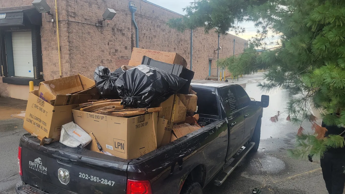Baten pickup truck loaded with broken-down cardboard and bagged waste at a commercial loading dock