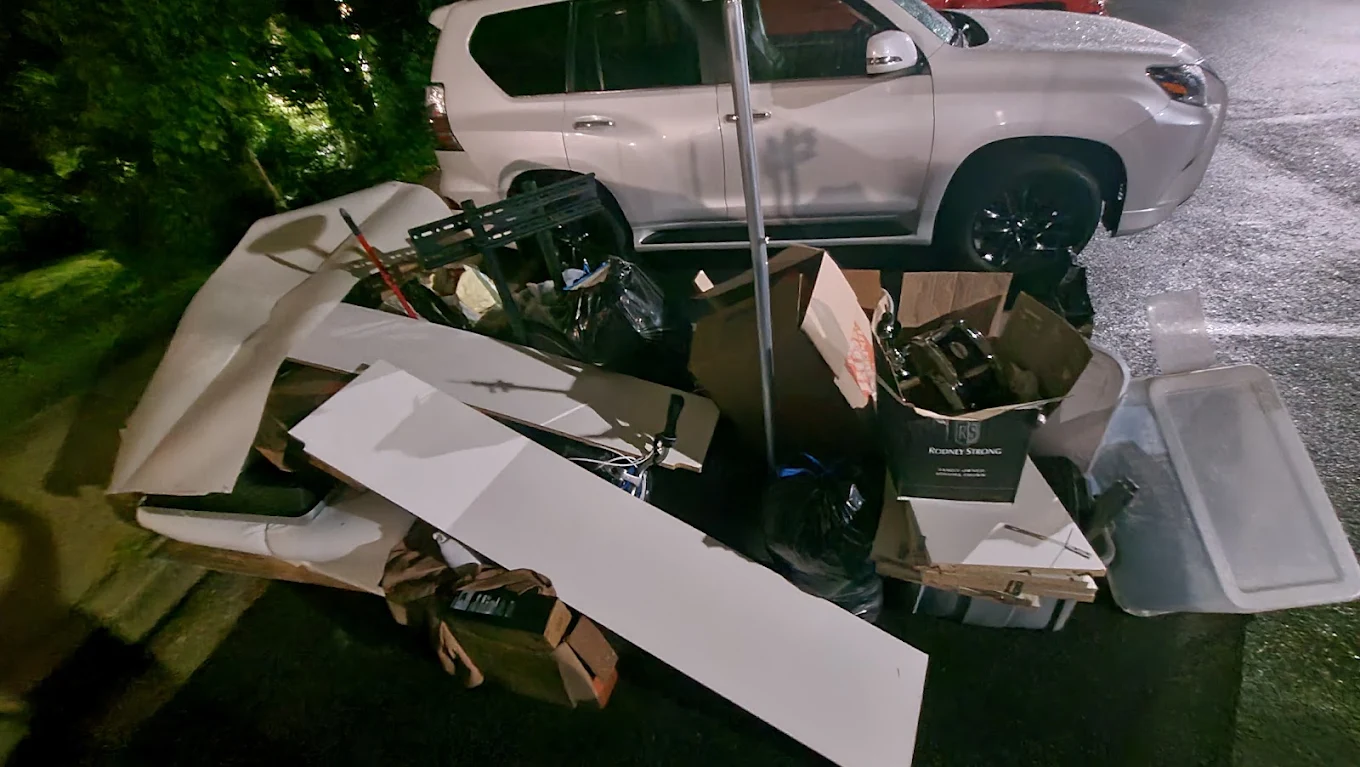Curbside pile of furniture, boxes and debris staged for junk removal at night