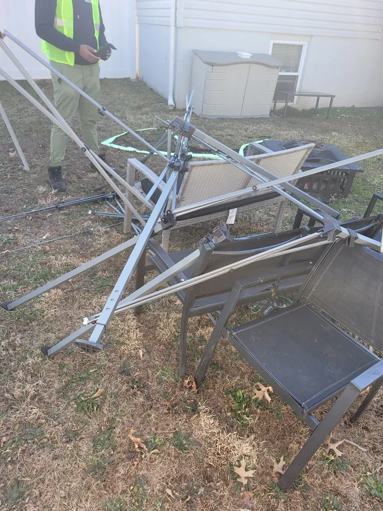Baten crew member in a safety vest disassembling a metal canopy and patio furniture in a backyard