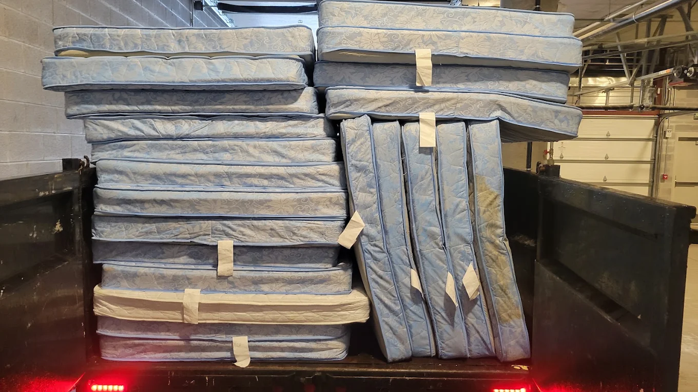Dozens of mattresses stacked wall-to-wall inside the Baten dump trailer in a building loading bay