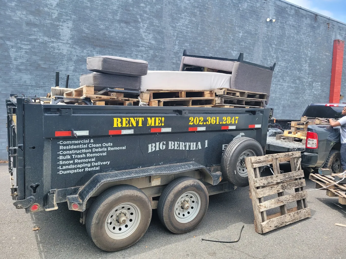 Dump trailer loaded with pallets and sofa cushions at a commercial site