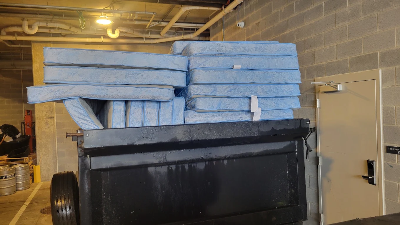 Dump trailer stacked high with blue mattresses inside a basement loading area