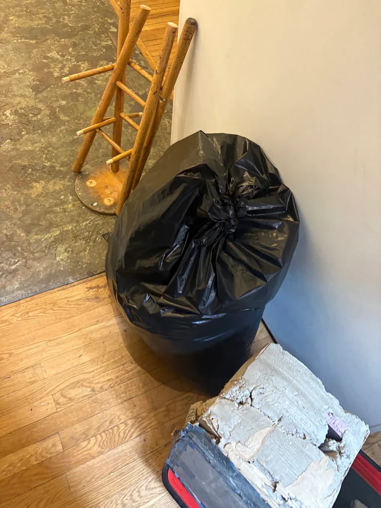 Bagged debris, a wooden stool and torn flooring in the corner of a room during a cleanout