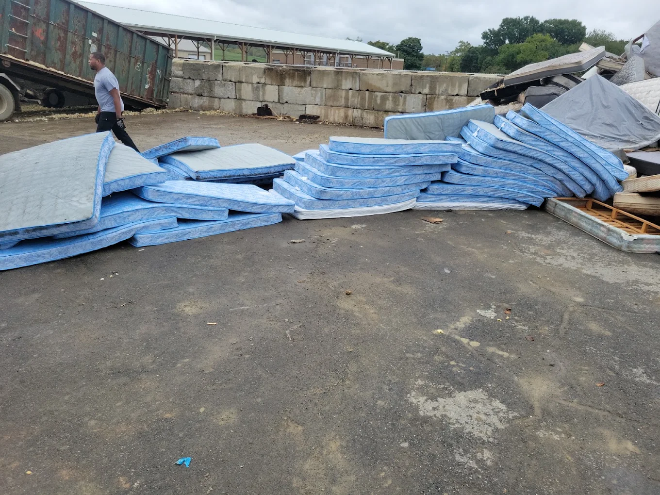 Baten crew member walking a yard of dozens of mattresses offloaded for recycling