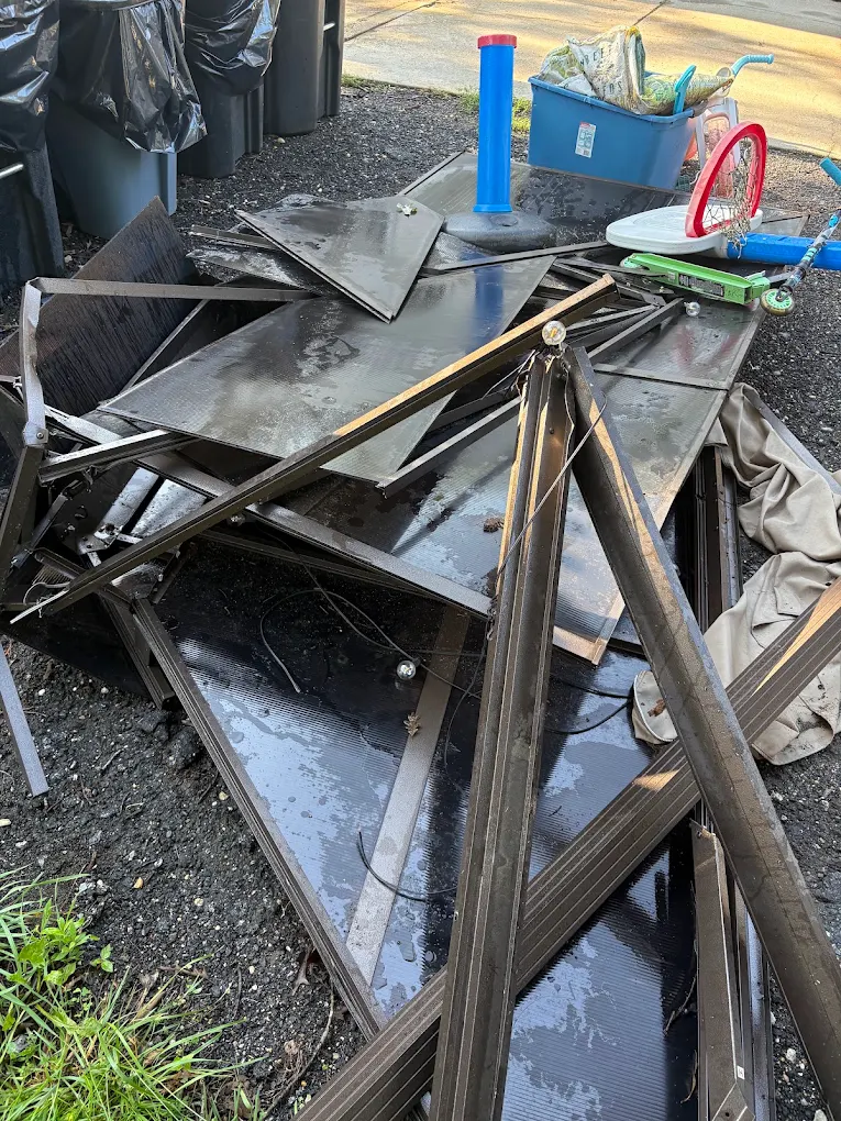 Demolished aluminum and polycarbonate sunroom panels stacked on a driveway after teardown