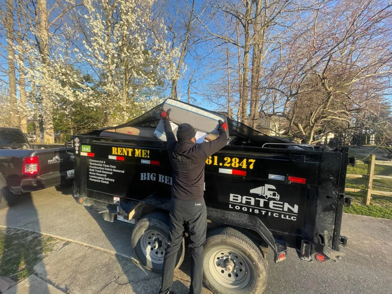 Baten crew member lifting a mattress over the rail of the Big Bertha 1 dump trailer on a spring morning