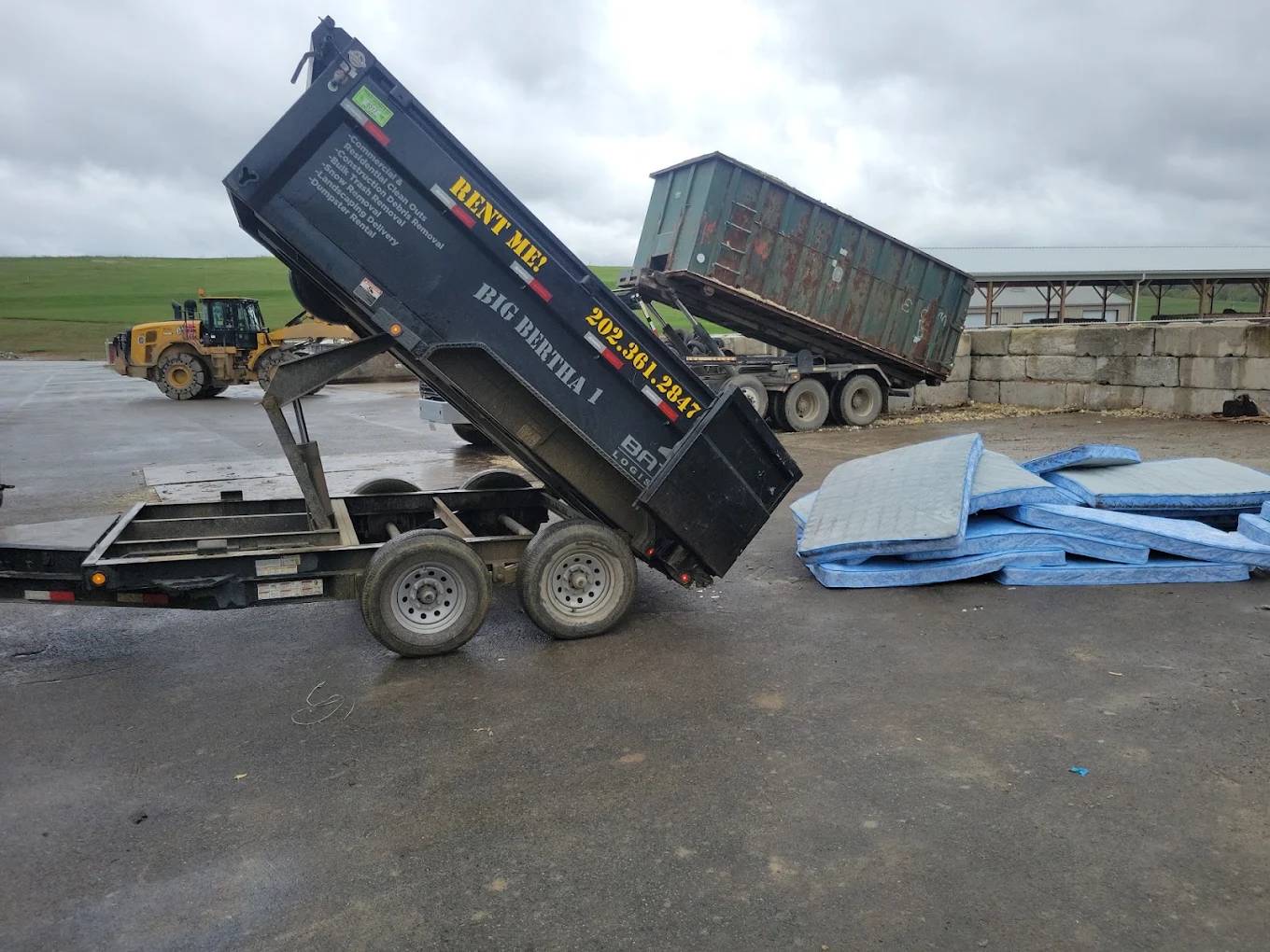 Big Bertha 1 dump trailer tipping a load at the transfer station beside a roll-off container
