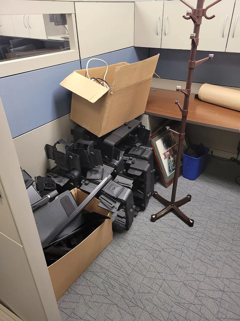 Office cubicle filled with stacked monitor mounts, cabling and boxed electronics during a decommission