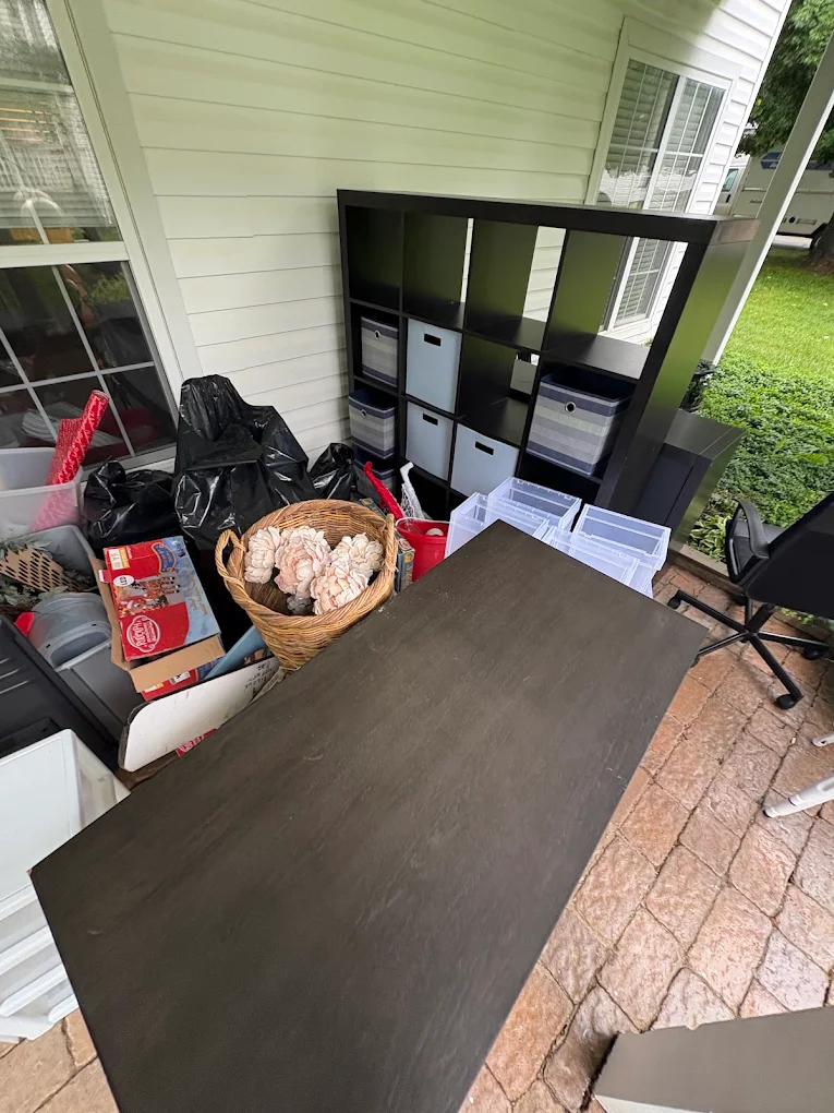 Patio staged with a cube shelving unit, table top, bins and bagged household items ready for pickup