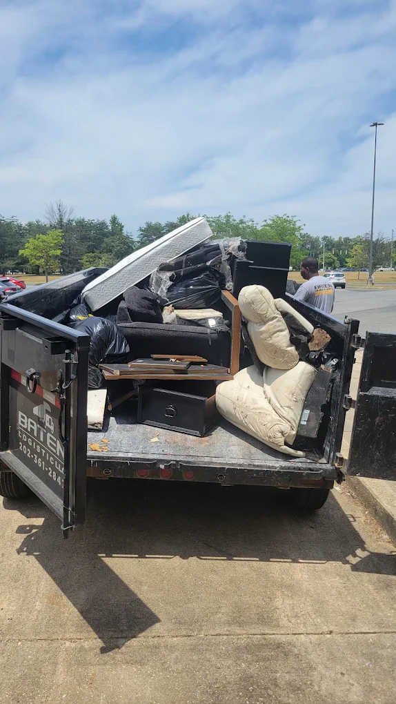 Baten dump trailer loaded with mattresses, recliners and bagged household junk in a parking lot
