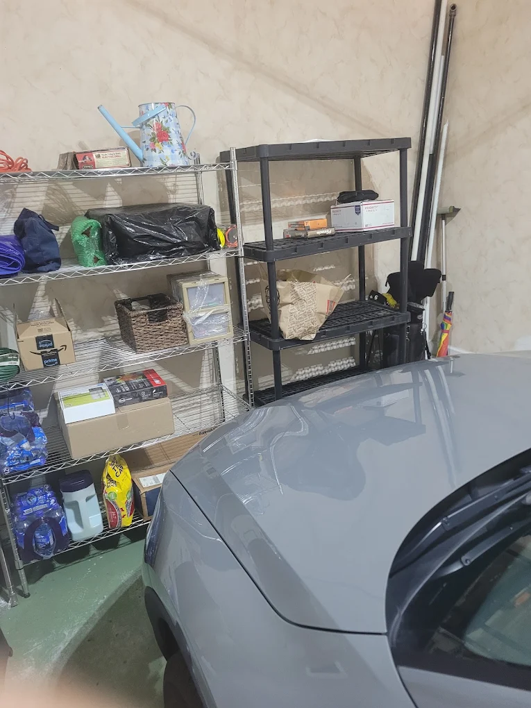 One-car garage with wire and plastic shelving, boxes and clutter squeezed beside a parked car